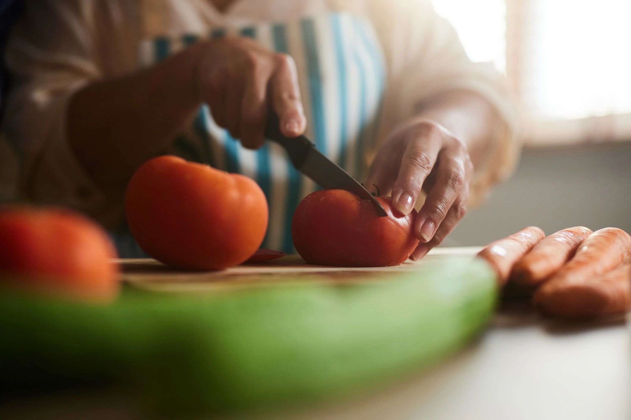 Hands chopping tomatoes on a cutting board in a kitchen